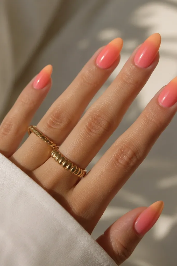 Almond nails with coral-pink base and a tangerine gradient that starts mid-nail and melts into a lighter peach at the very tip; glossy finish.