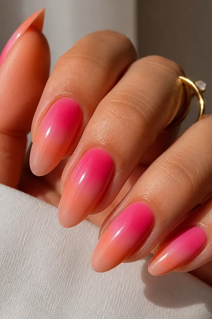 Long almond nails with a nude pink base. The inner area near the cuticle is hot pink, fading out into a coral orange halo toward the sides and tips. The aura is sharpest at the center and softer at the edges, with a glossy finish.