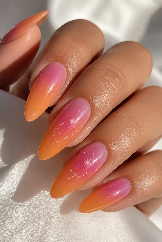 Long almond nails. Pink aura fades into orange with a glazed, high-shine finish. On two nails, tiny white dot stars sit near the aura center, spaced like little constellations. The rest is clean and glossy.