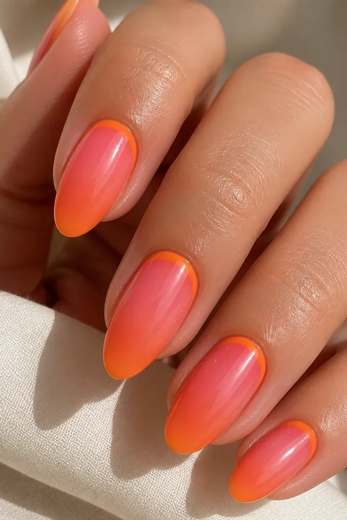Medium almond nails. A rosy pink aura spreads across the nail, and a curved orange crescent sits just under the cuticle line, blending outward. The rest transitions softly into orange toward the tip. Glossy finish.