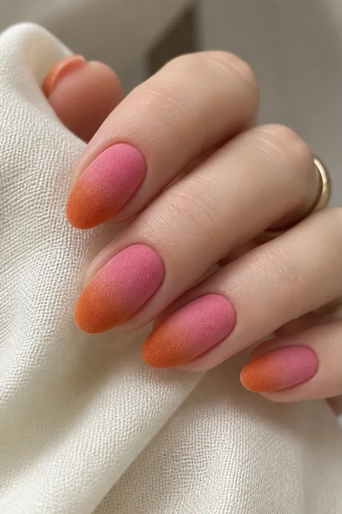 Short almond nails. The aura is pink fading into orange, but the finish is velvet/velour - not glossy. The orange area looks slightly darker and velvety, with a soft matte texture and no extra gems.