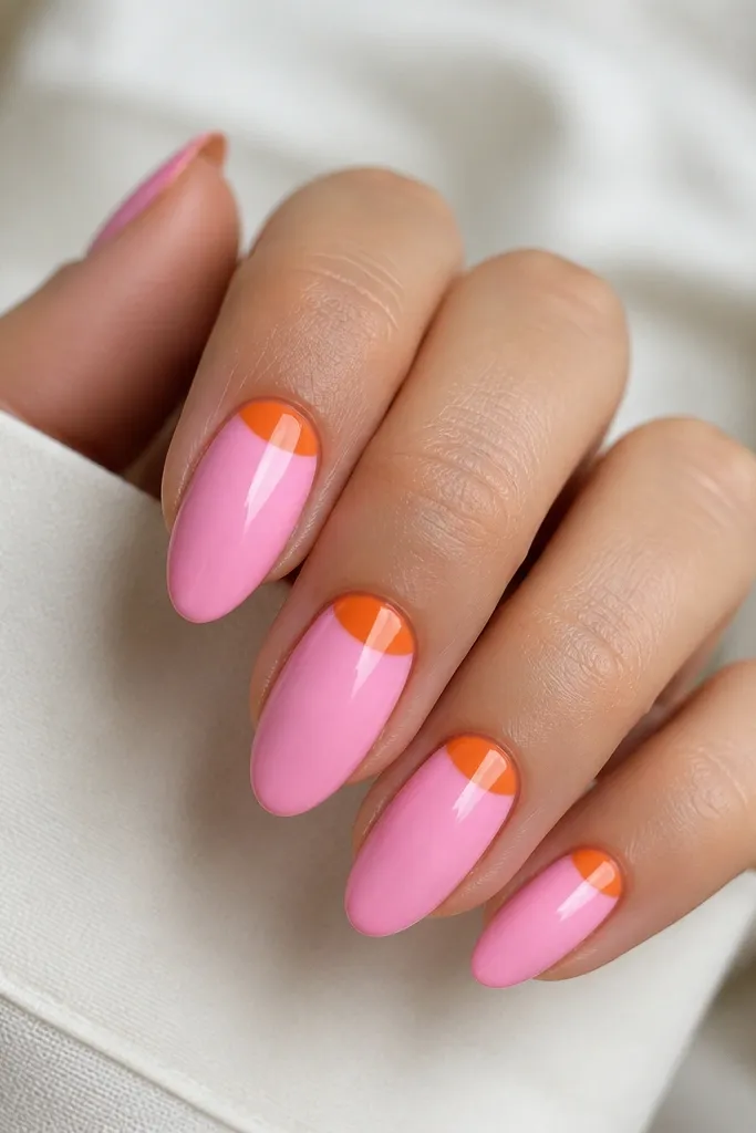 Medium-length almond nails. The base is opaque bubblegum pink. At the cuticle, each nail has a crisp half-moon of tangerine orange that curves neatly under the nail plate. Glossy top coat, clean cuticle line.
