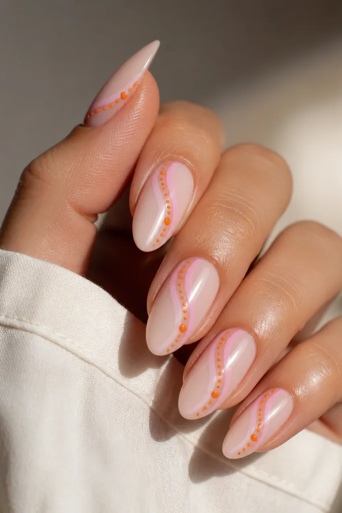 Medium almond nails with a glossy pink swirl across the center of each nail. The background is milky nude-pink. On the swirl tail, there are tiny clusters of orange dots, three to five dots each, with a single larger dot at the end.