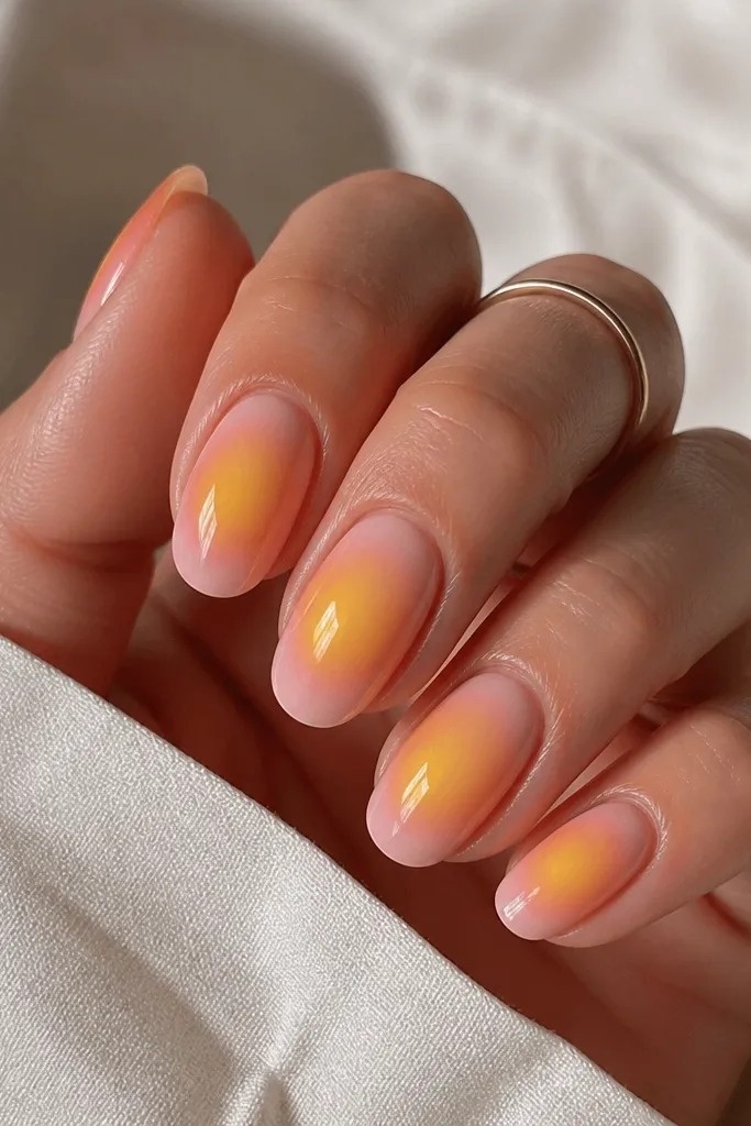 Medium oval nails with a soft airbrushed aura effect. The outer edges fade from milky pink into orange, and the center has a bright yellow glow circle.