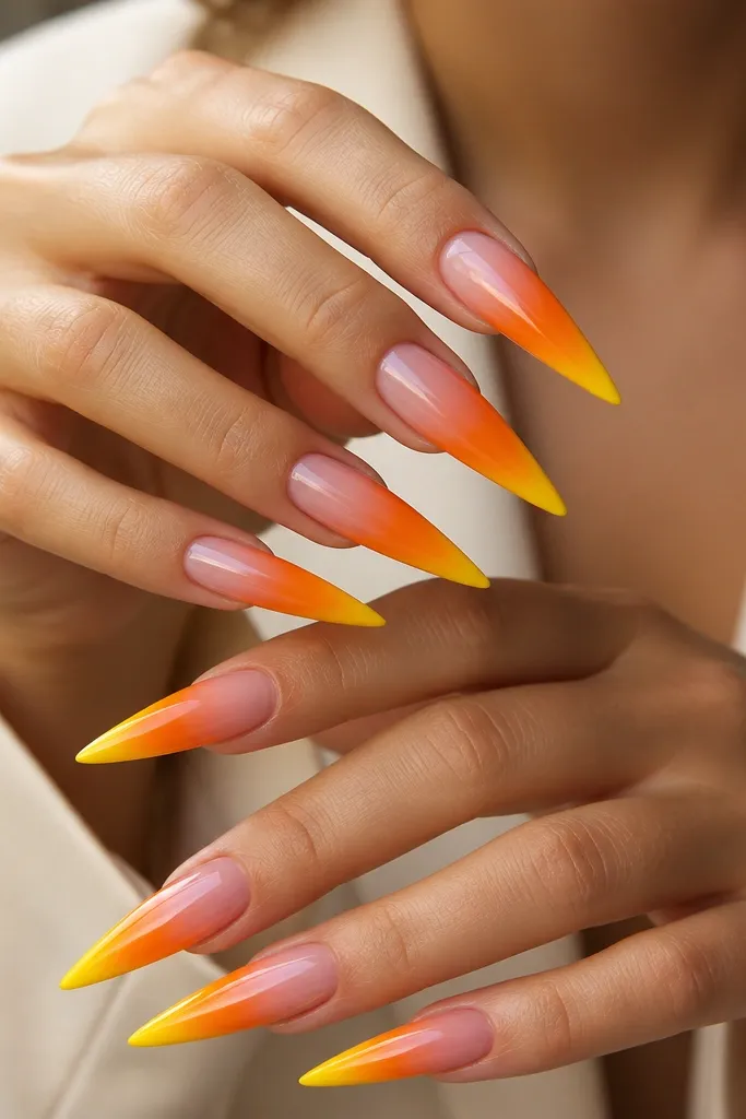 Long stiletto nails with a smooth ombré from sheer pink at the cuticle to orange in the middle. The very tip is solid yellow with a glossy finish.