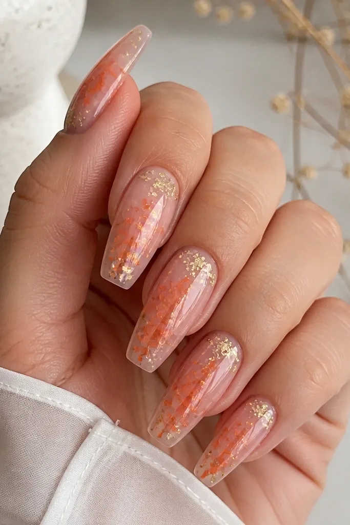 Medium coffin nails with a clear-pink glassy base. Orange confetti flakes are scattered across the center, and tiny yellow foil flecks catch the light near the cuticle.