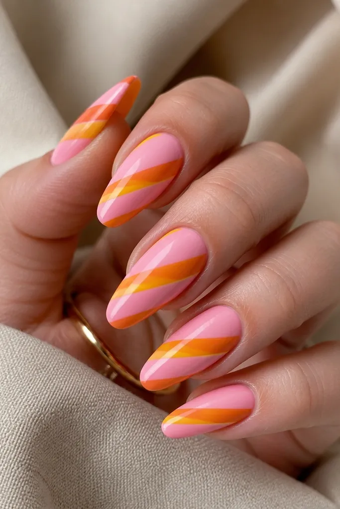 Long almond nails on a glossy pink base. Diagonal stripes run from lower left to upper right in alternating orange and yellow, with clean edges.