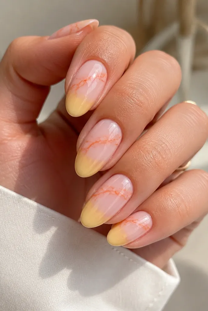Medium almond nails. The base is milky pink marble, orange veins run mostly across the top half, and the tips are painted yellow with a soft edge.