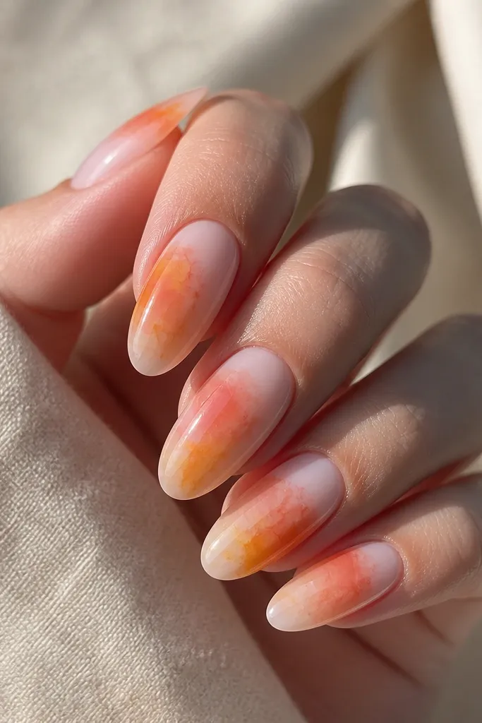 Long oval nails with a milky pink base. Orange and yellow watercolor washes spread like paint in water, with soft edges and no hard lines.