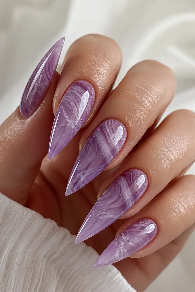 Stiletto nails with a swirled grape marble base. Shell ridges appear as curved semi-transparent lavender lines. White wave-like veins run through the ridges and blend softly into the background. Gloss finish.