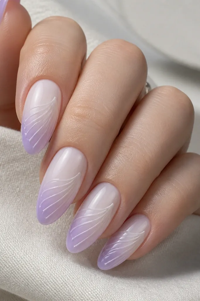 Long oval nails. Ombre fades from milky white near the cuticle into soft lavender at the tip. Shell ridges appear as slightly darker lavender curved lines across the nail. A milky white crest line runs along the outer ridge edge.