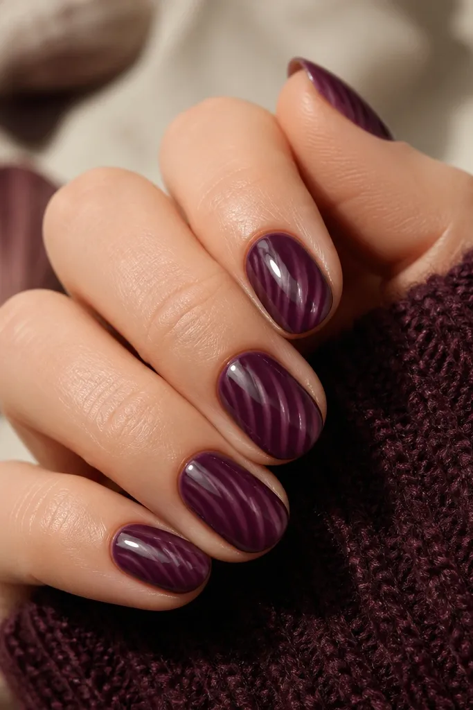 Short almond nails. Base is deep plum. Shell ridges are a lighter plum drawn in curved lines. The topcoat looks jelly-like and slightly translucent, making the ridges look suspended.