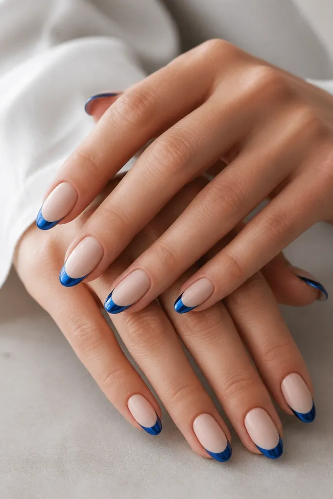 Medium almond nails with matte nude base; blue chrome French tips are glossy mirror; no rhinestones, just the contrast; clean, sharp smile lines.