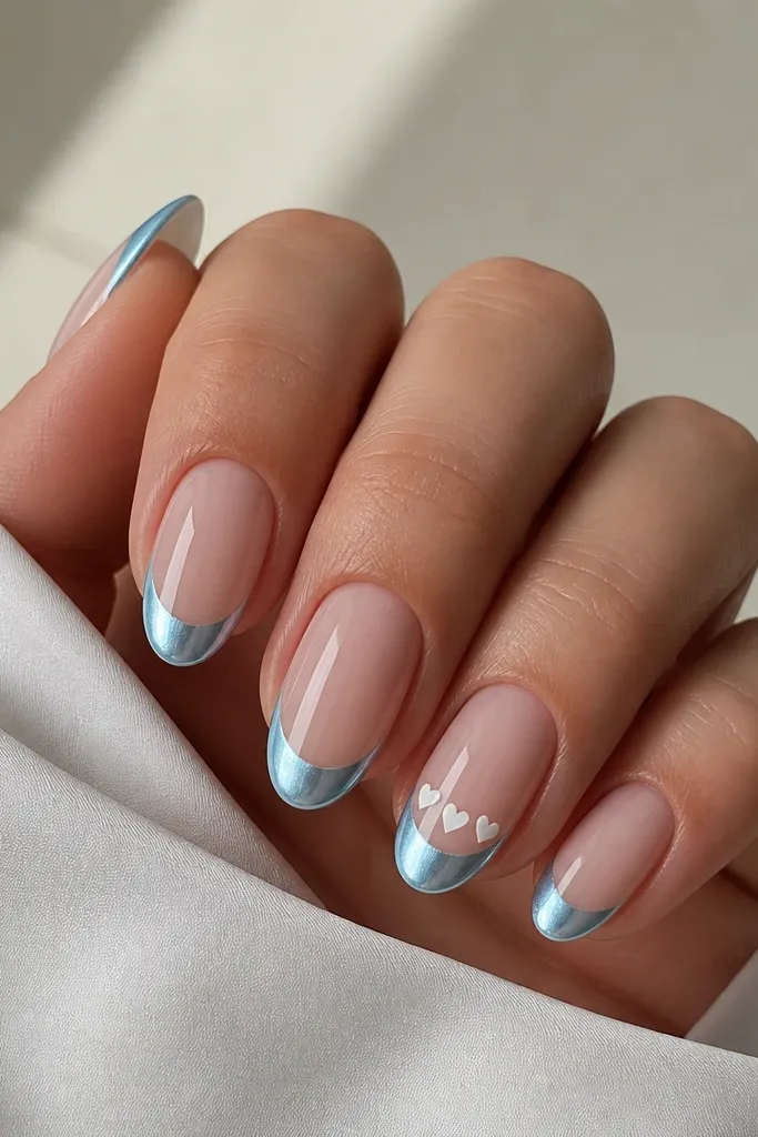Medium almond nails with icy blue chrome French tips; ring finger has three tiny white micro hearts spaced in a horizontal line just under the blue curve; other nails are plain chrome French; glossy mirror.