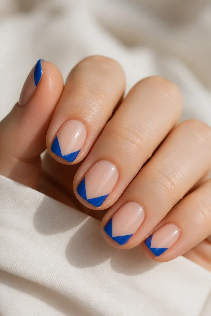 Short nails with a glossy clear nude base. The French tip is royal blue but split by a clear V-shaped negative space in the center, pointing toward the free edge. The blue sides are smooth and glossy, meeting the V at crisp angles. No glitter - just sharp geometry.