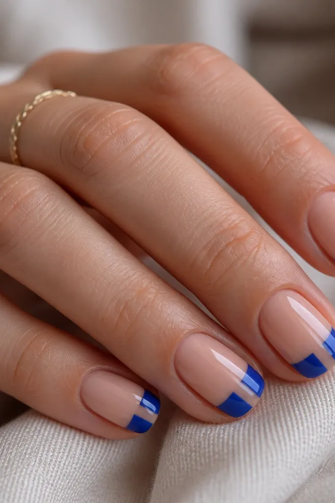 Short nails with glossy nude base. The French tip is royal blue on both sides, but the center strip of the tip is clear jelly - you can see the nude beneath through it. The clear strip is straight and centered, with clean edges where it meets the blue. The overall look is glossy and dimensional.