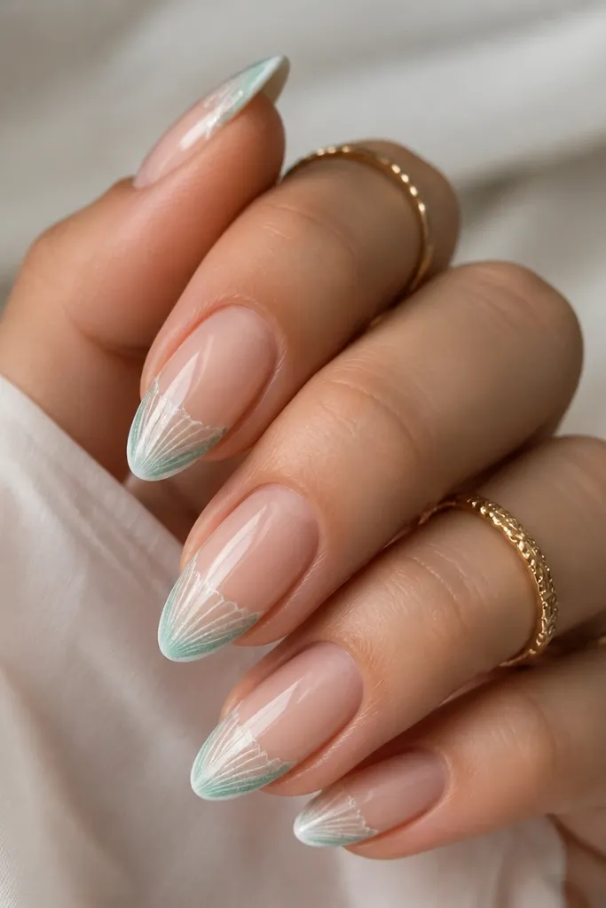 Almond nails with a sheer nude base. French tips are white in the center, fading into a soft teal at the outer corners. Inside the tip, there are faint shell ridges in off-white and teal shimmer.