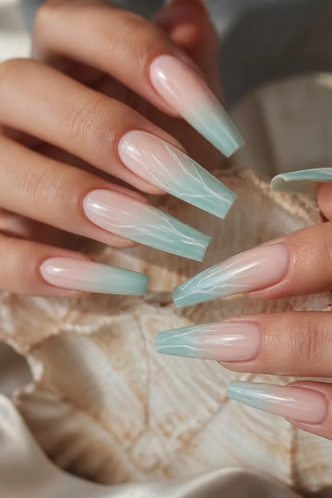 Long coffin nails with a smooth gradient from pale nude at the cuticle to seafoam green at the tips. Over the gradient, thin white lines curve like shell veins across two accent nails and lightly across the rest. The seafoam looks airy and translucent, and the nails are mirror glossy with no heavy glitter.