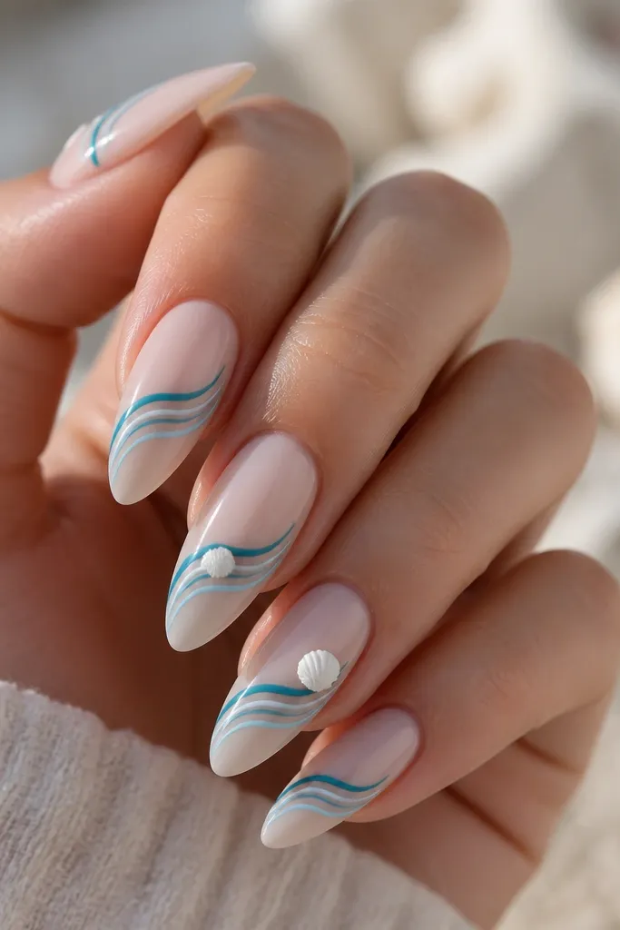 Long almond nails with a glossy nude base. Across each nail are thin ocean wave lines in teal and pale blue, drawn diagonally. On two nails, tiny shell beads in white sit at the wave peaks like small pearls. The wave lines are crisp and the finish is glassy.