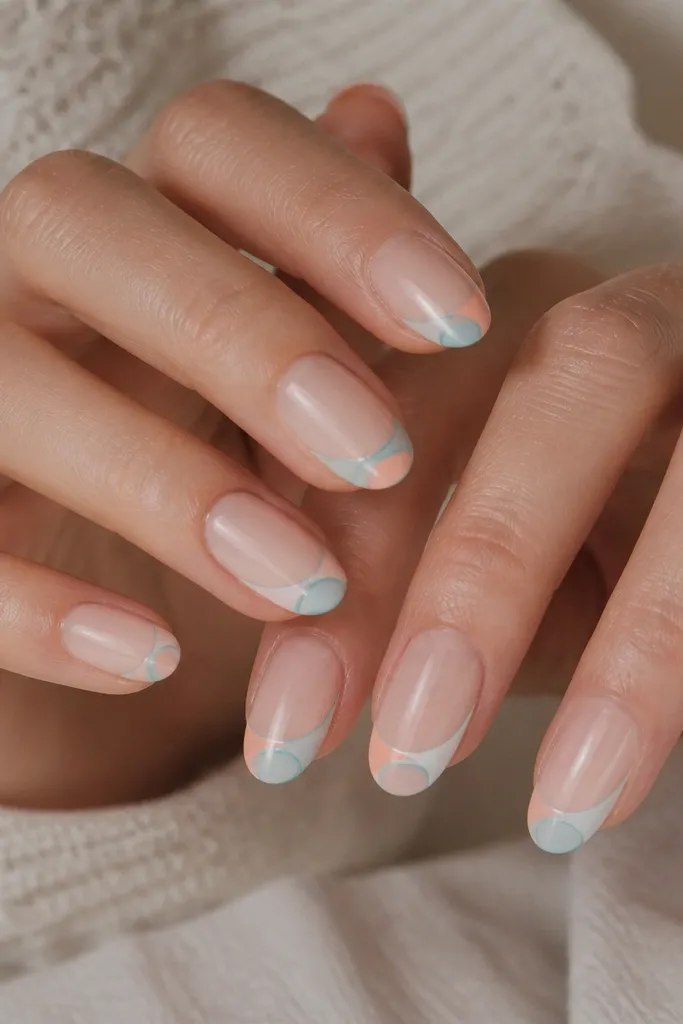 Nails are sheer nude. Each nail has two overlapping half-moon shell shapes near the tip: one in pale peach, the other in milky white with a thin teal outline. Glossy finish.