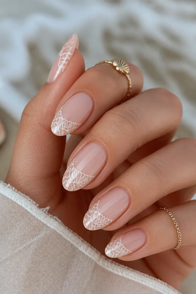 Nails are sheer nude with negative space. On the ring fingers, a lace-like shell pattern is drawn in thin white lines with small scallop edges. Other nails stay plain nude.