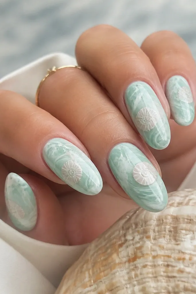 Nails have seafoam marble swirls in mint and white. On each nail, there is a faint shell swirl drawn in pale pink and a small white highlight ridge.