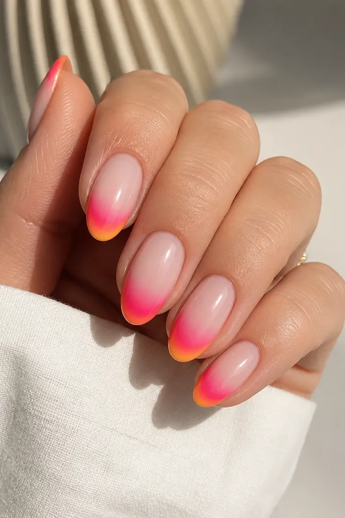 Short almond nails with a nude base; tips fade from pale peach into hot pink and then a soft orange at the very edge; glossy gradient looks smooth.