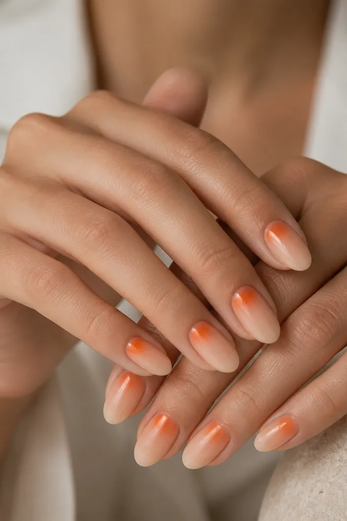 Short almond nails with a sheer nude base; a tangerine half-moon sits at the cuticle and fades outward into a soft gradient toward mid-nail; glossy.
