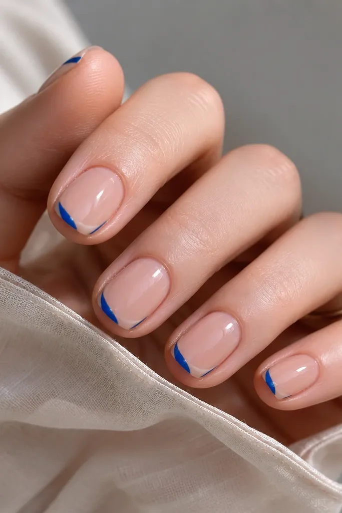 Short nails with nude base. The French tip is blue but only covers the outer edge, leaving a negative space half-moon near the center of the tip. Glossy finish.