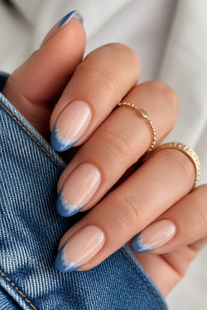 Short almond nails. Nude base. Denim blue French tips with a soft, feathered white watercolor blend at the outer edge. Glossy finish.