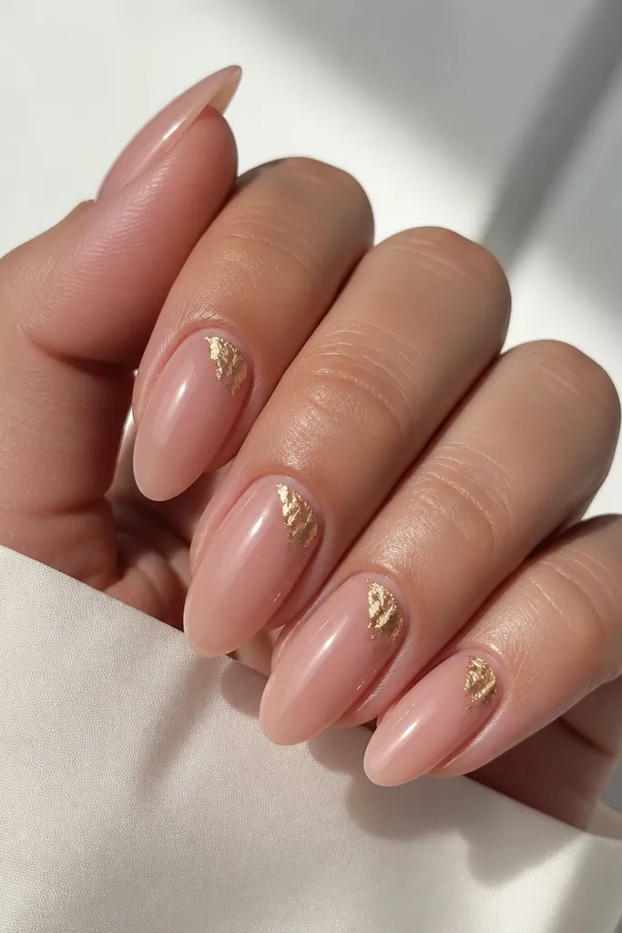 Almond nails with a peach jelly pink base that shows a hint of natural nail through. On the top outer corner of each nail, there's irregular gold foil laid like a small accent triangle. Everything is glossy.