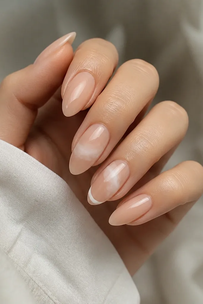 Almond nails with a nude base. On two accent nails, there's a soft white cloud-like swirl near the middle and a tiny curved line near the tip. The rest of the nails are plain glossy nude.