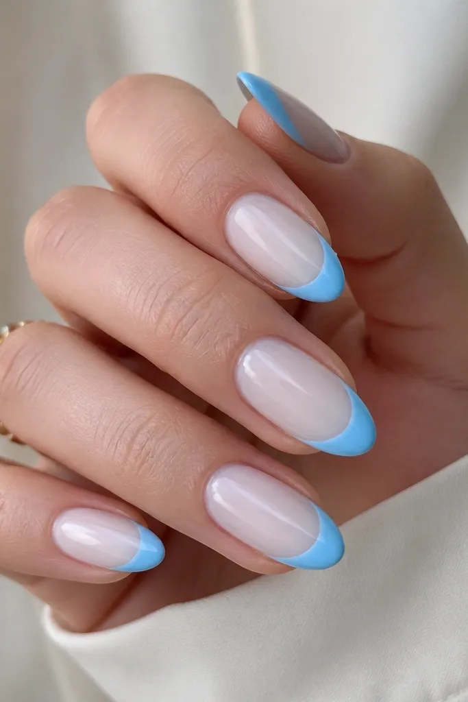 Medium almond nails with milky white base (slightly sheer). French tips are sky blue with a smooth curve and medium thickness. The tips are glossy and evenly opaque, with a clean border at the sides.