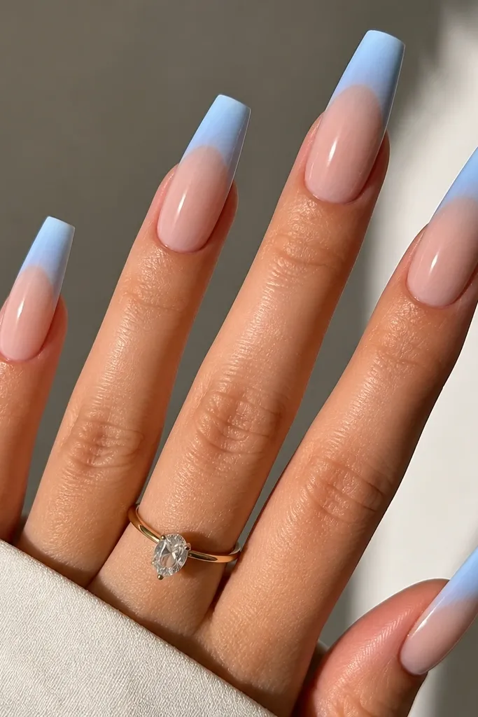 Long coffin nails with sheer nude base. French tips blend from light icy sky blue at the edge to slightly deeper blue toward the center, forming an ombre French. Glossy finish, no glitter.