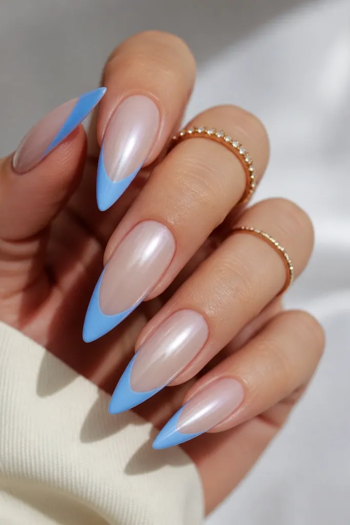 Stiletto nails with pearly nude base that shifts slightly. French tips are sky blue, medium thickness, with a sharp smile line. High gloss topcoat, clean cuticle area.