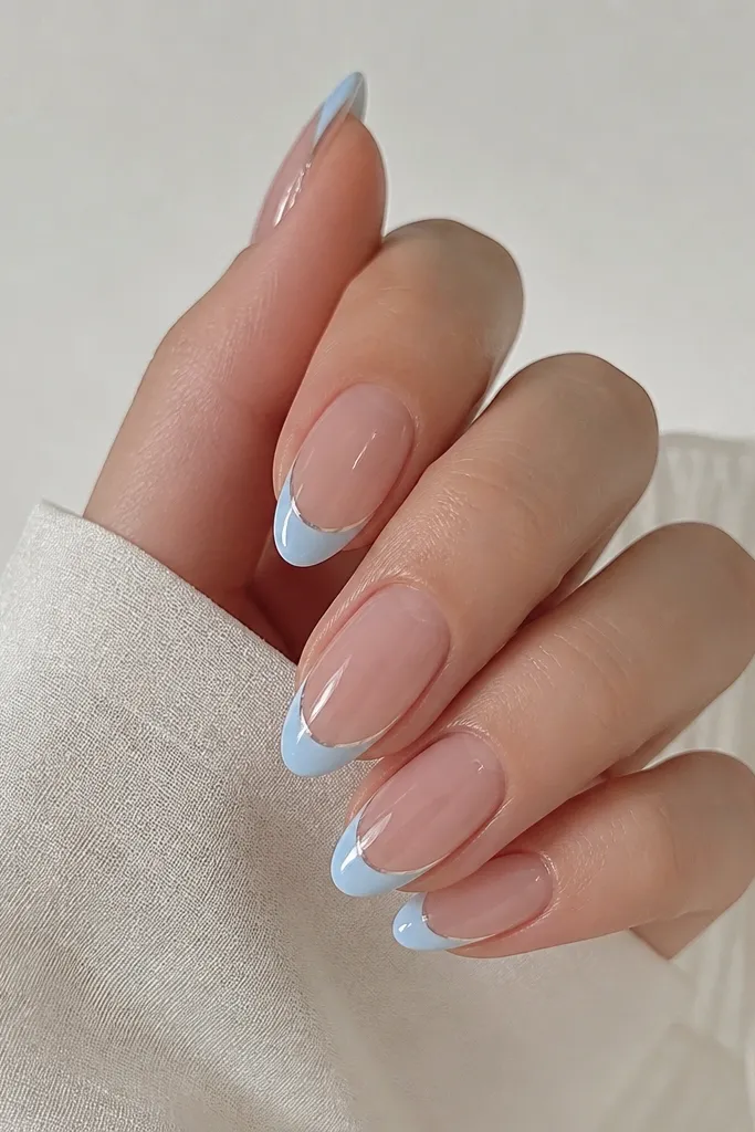 Medium almond nails with sheer nude base. Sky blue French tips have a glossy, crystal-clear overlay band right along the smile line. The overlay is transparent and catches light, making the curve look sharper.