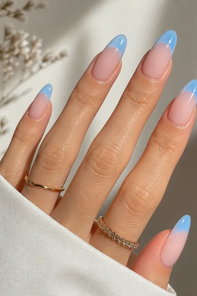 Long oval nails with sheer nude base. Sky blue French tips are glossy. In the center of the tip area, there's a soft aura glow that fades outward, like a light halo in sky blue.