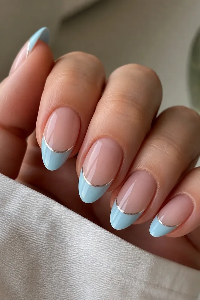 Medium almond nails with sheer nude base. Sky blue French tips are glossy. A thin silver chrome half-moon sits right under the smile line on each nail, centered.