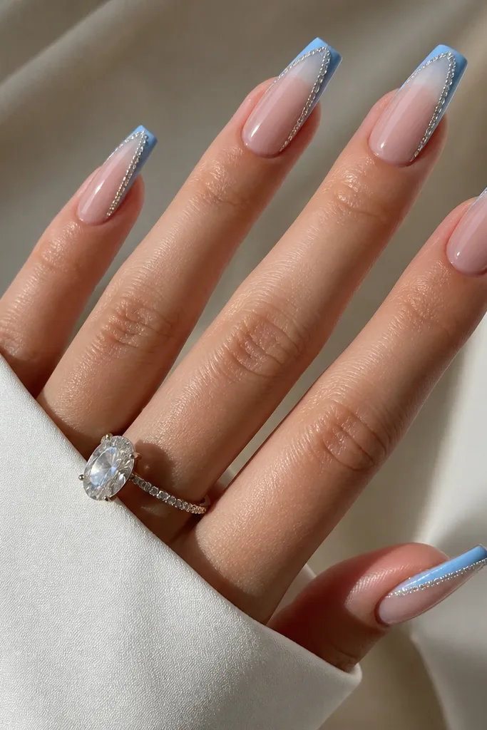 Medium coffin nails with sheer nude base. French tips are glossy sky blue. Along the outer edge of the tip on each nail, there's a thin strip of tiny clear rhinestones set in a line. Clean cuticle, bright sparkle.