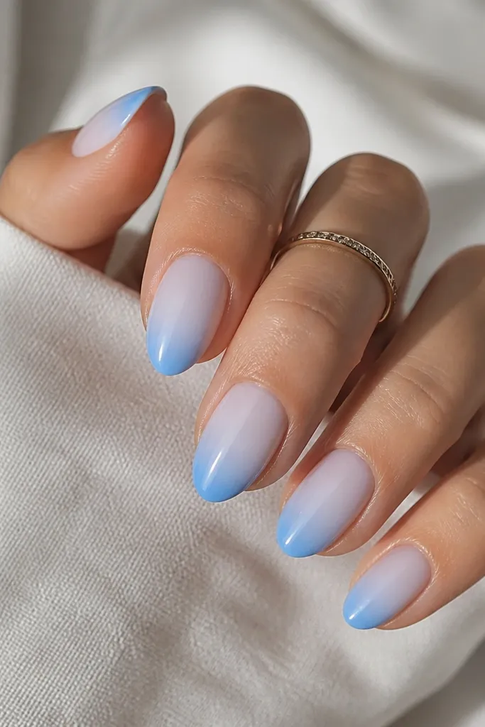 Short almond nails with a light sky blue fade starting near the cuticle and transitioning into a stronger sky blue at the French tip. The base is not fully nude; it's a smooth gradient into the tip.