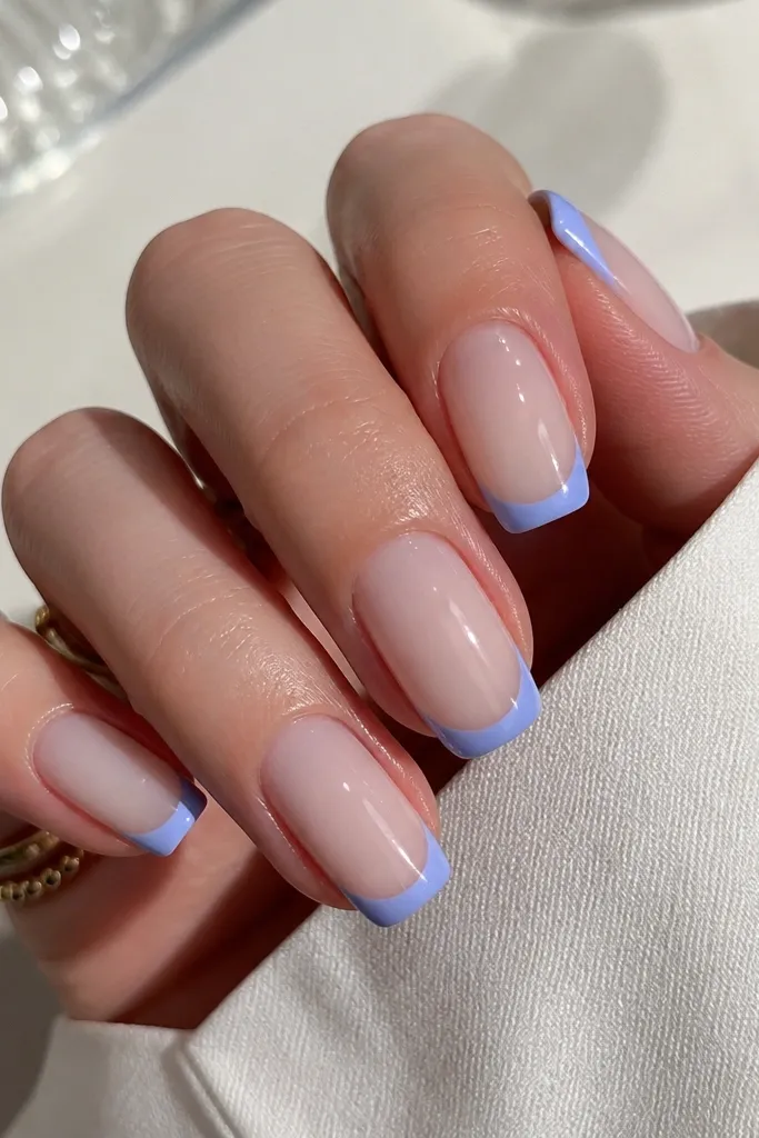 Medium squoval nails with a milky nude base. The French tips are periwinkle blue, slightly thicker than a micro line, with a soft curved edge and a glassy shine.