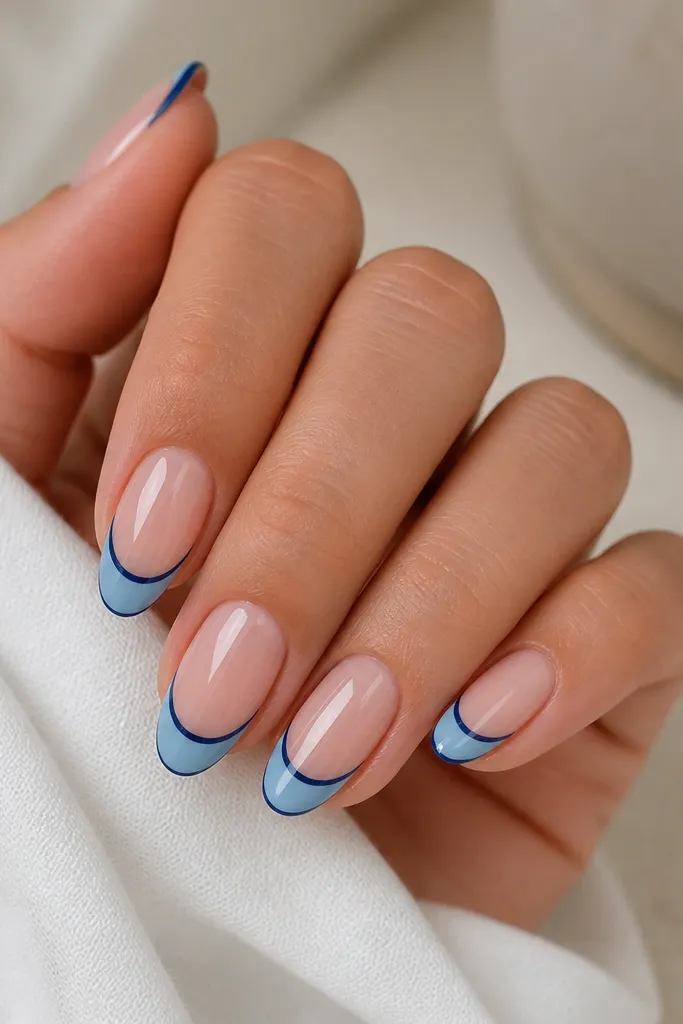 Nails with a sheer nude base. The tip has a thin navy outline following the French smile, and the inside of the tip is filled with a lighter sky blue. The outline is crisp, and the fill looks smooth and opaque under a glossy top coat.