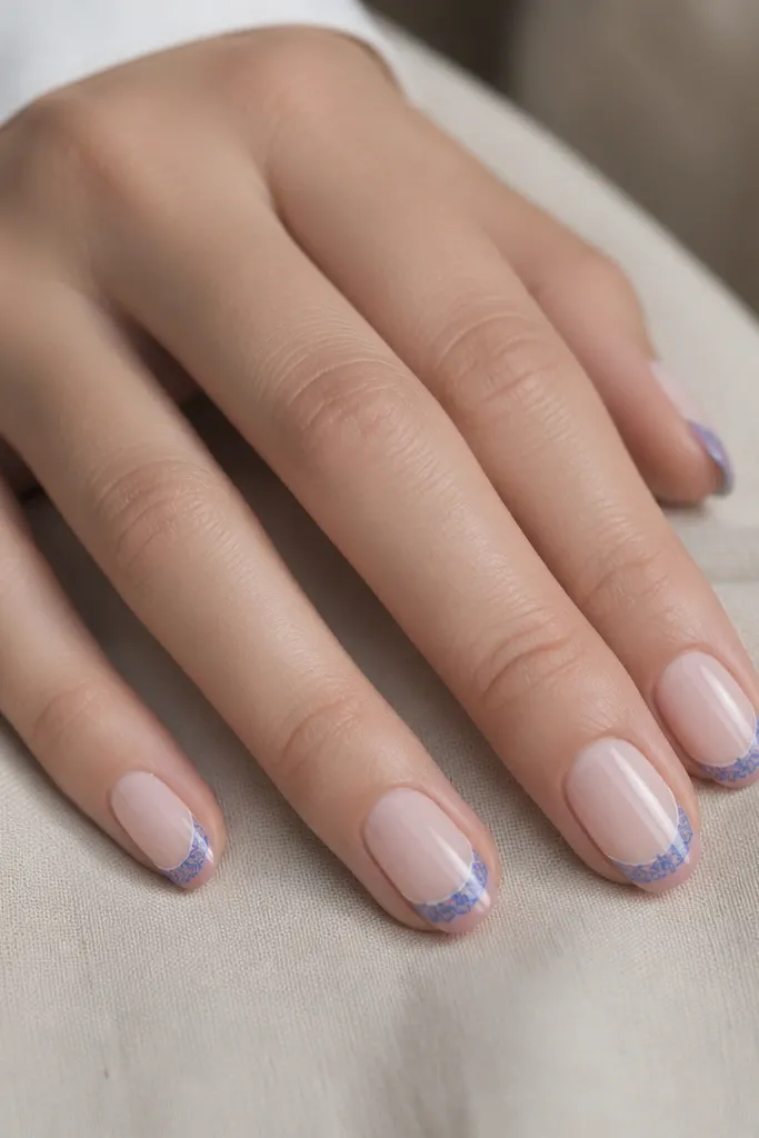 Sheer nude nails with a small negative-space border near the tip. A delicate pattern of blue lines appears only on the tip area, like tiny lace, with a glossy finish.
