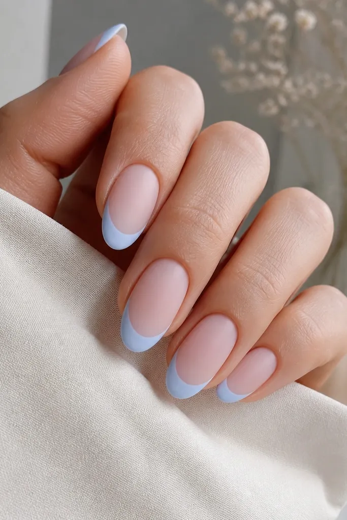 Nails with a sheer pink base and baby-blue French tips. The tips look slightly powdery, and the finish is matte, not glossy, with soft edges and a smooth surface.