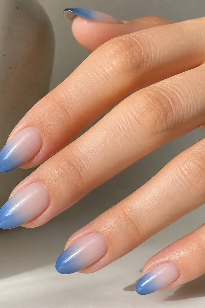 Nails with a sheer nude base that fades upward into a blue tip. The blue is strongest at the free edge and gradually fades toward the nail bed, with a smooth gradient. Glossy finish.