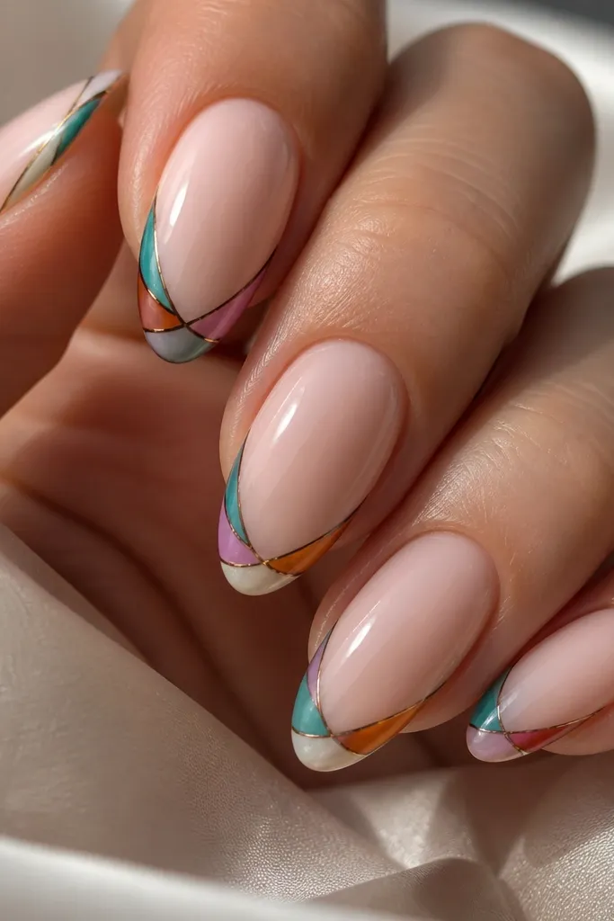 Close-up of almond nails on a hand: milky nude base, French tip with thin curved lines in teal, amber, and soft violet, like stained glass. High-gloss top coat reflects light.