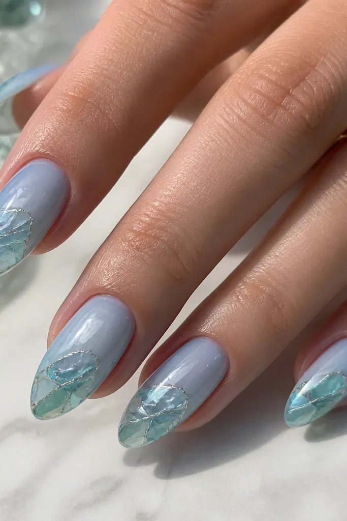 Almond nails in a cool ocean blue sheer base. The tips have translucent sea-glass panels in aqua and icy green with irregular edges, sealed under glossy top coat.