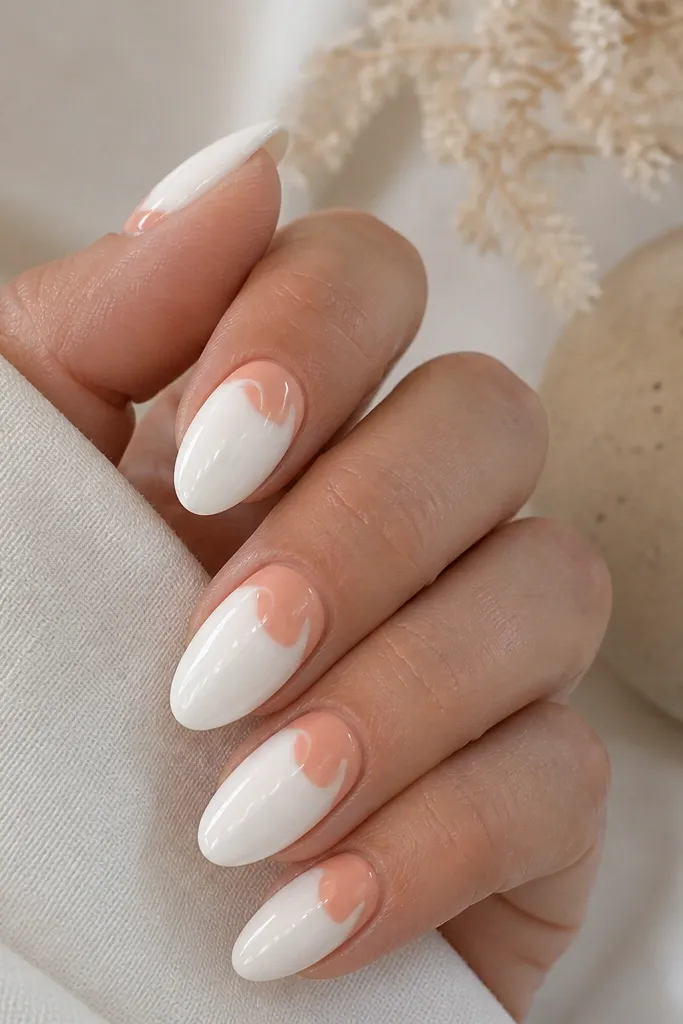 Almond nails painted in opaque white milk gel. A peach brushstroke sits right above the cuticle and curves outward, leaving the rest mostly white. Glossy top coat.