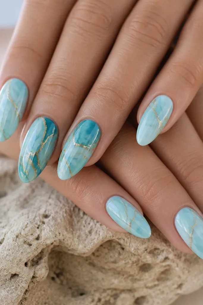 Almond nails with turquoise and icy blue marble swirls. Thin gold crack lines run through the marble like cracks in stone. Glossy finish.