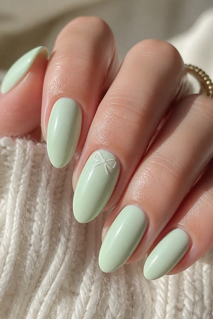 Almond nails in mint cream pastel. On one nail there is a tiny white bow tie accent near the cuticle, outlined with a thin mint line. Glossy finish.
